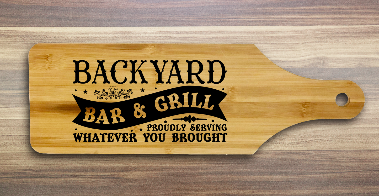 A laser engraved bamboo charcuterie board with the saying Back Yard Bar & Grill proudly serving whatever you brought.