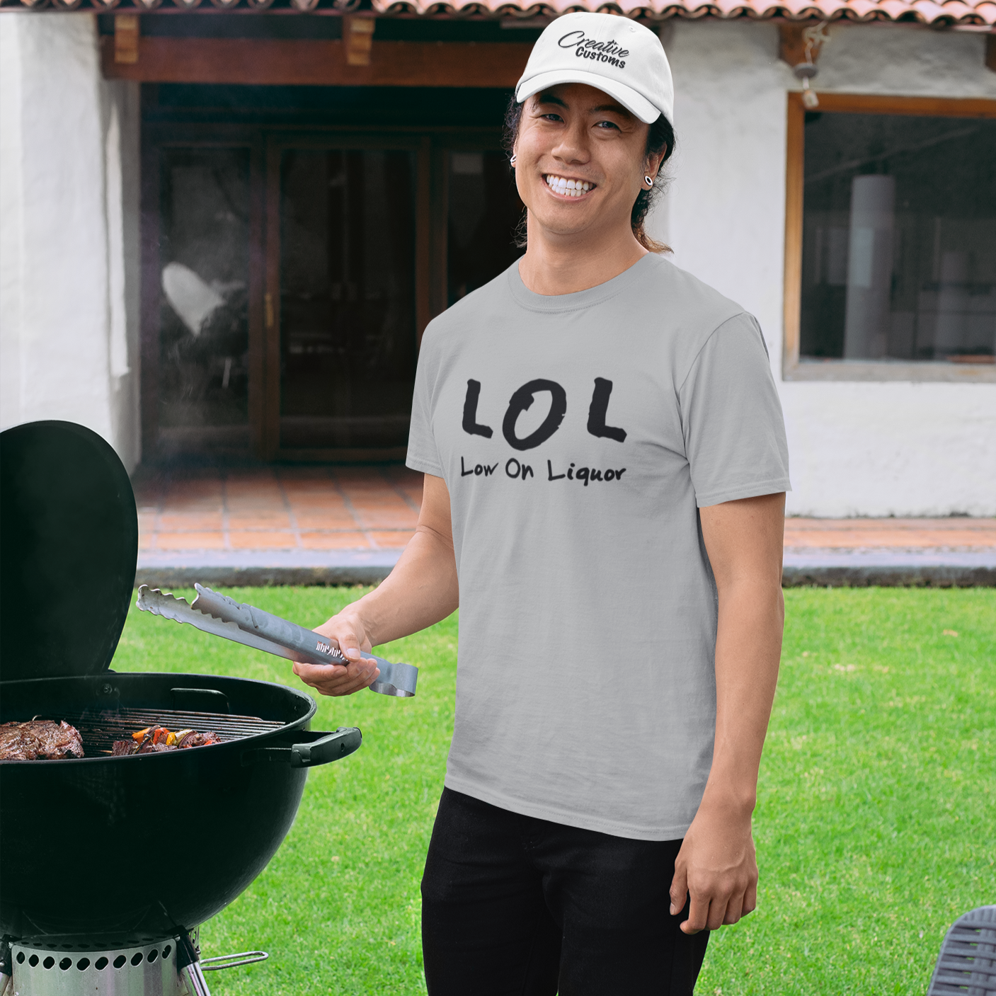 A man standing at a bbq smiling wearing a grey t shirt that says LOL low on liquor