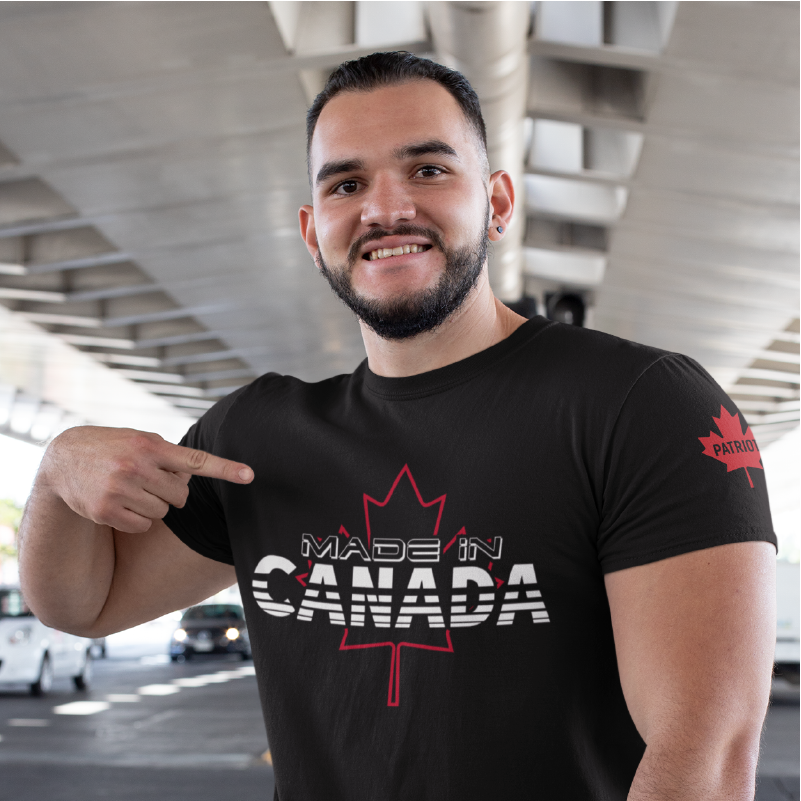 A man pointing at himself, wearing A black t-shirt with a Canadian maple leaf on the front chest that says made in Canada and a maple leaf on the left sleeve with the word patriot