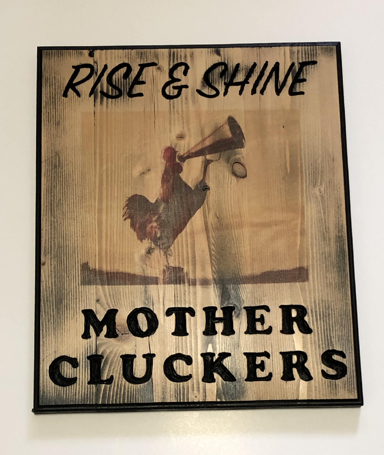 A hand routed wood sign with a rooster with a horn and the words Rise And Shine Mother Cluckers