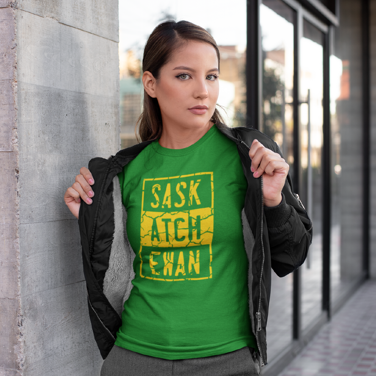 A young woman flashing open her jacket to show off a green t-shirt with a yellow compton style Saskatchewan graphic on the front chest