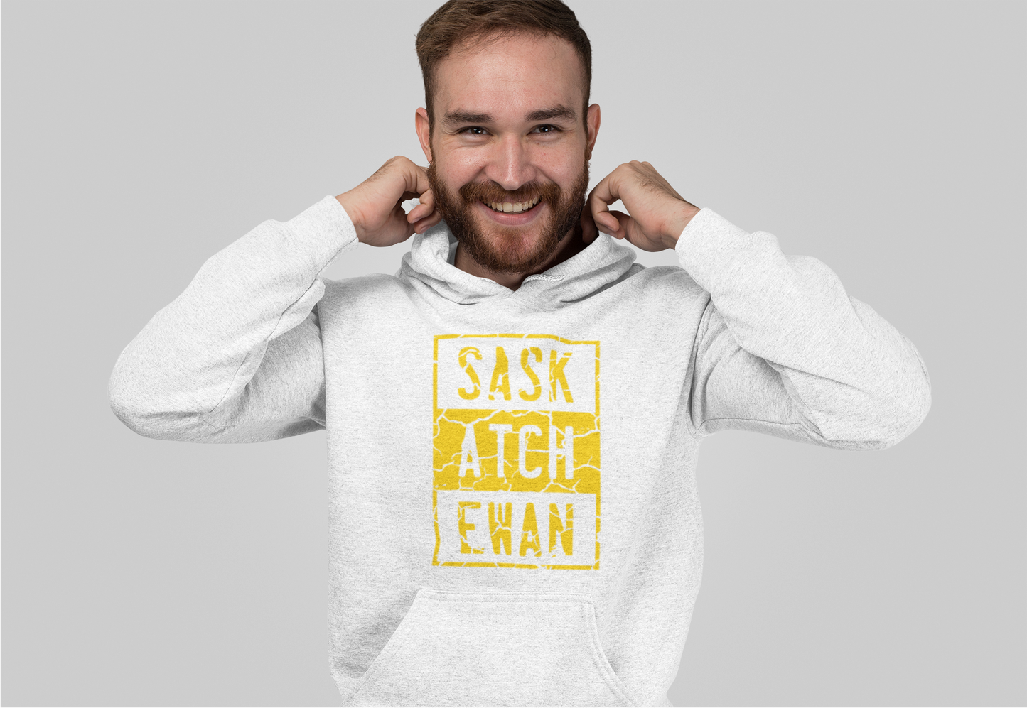 A man pulling up the hood on a pullover hoodie  with a yellow compton style Saskatchewan graphic on the front chest