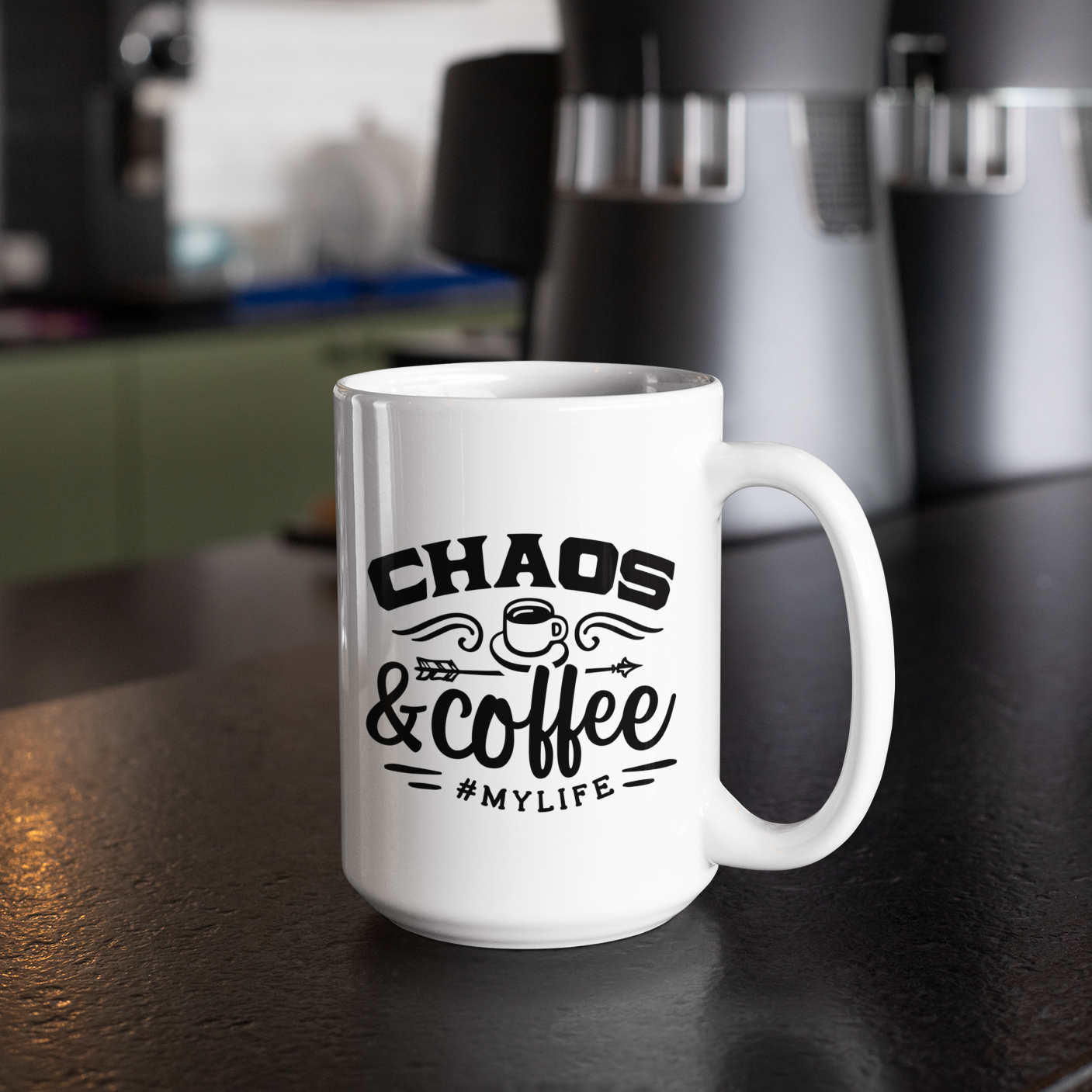 A white 15oz coffee mug with black writing sitting on a counter with a coffee maker in the background that says, chaos & coffee #mylife