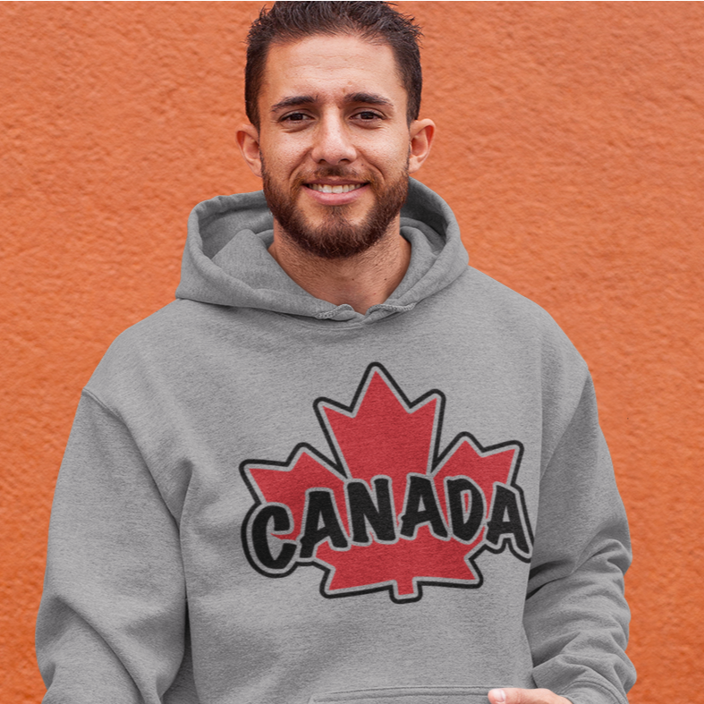 A man smiling standing infant of a orange wall wearing a grey heavy hoodie with a Canadian maple leaf and the word Canada on the chest