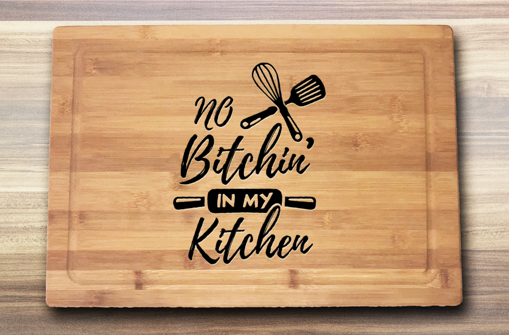 laser engraved bamboo cutting board with the saying no bitcin' in my kitchen with a rolling pin and some kitchen utensils 